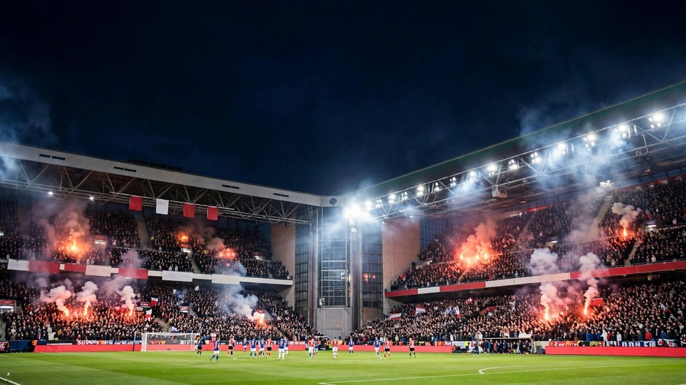 Voetballer schiet op doel in een vol stadion tijdens een avondwedstrijd
